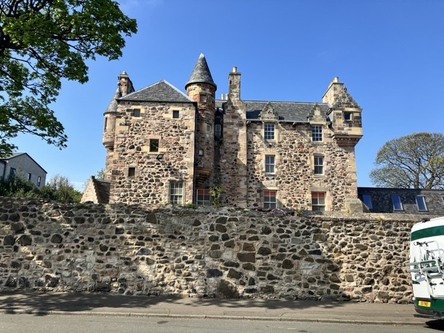 An old Scottish Baronial house with turrets,built of stone of irregular shape and many colours, against a blue sky